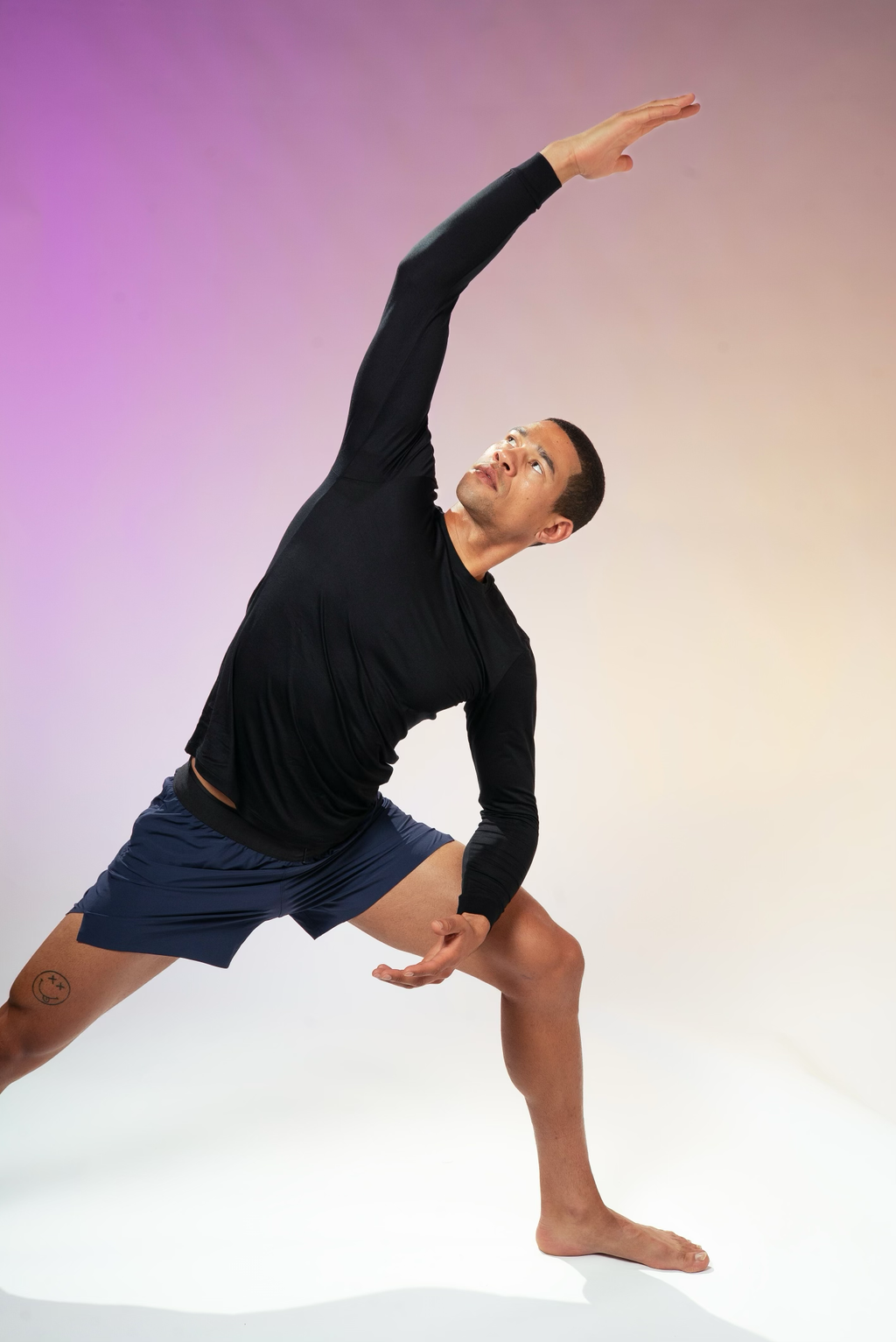 An athletic man, possibly a yoga instructor, demonstrates a pose. He's wearing a dark top and shorts, against a neutral background, emphasizing the focus on his form. 